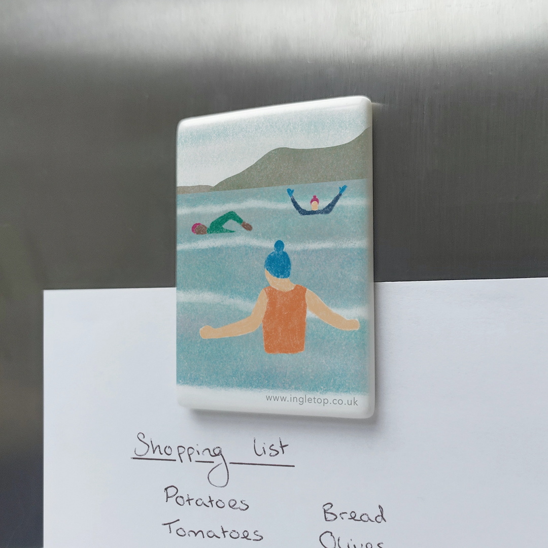 A fridge magnet with an illustration of a group of people wild swimming in an outdoor body of water, wearing bobble hats and swim gloves.