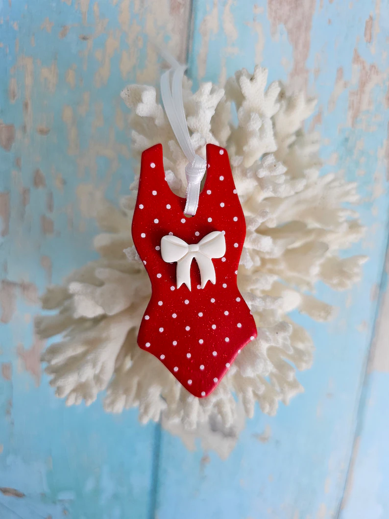 Handmade red polka dot swimsuit decoration with white bow and white satin ribbon, displayed on coral – unique swimmer ornament or gift.