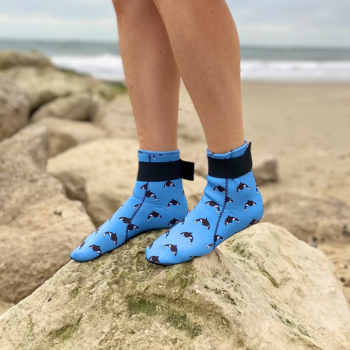Person wearing blue neoprene socks with dog pattern on a rocky beach