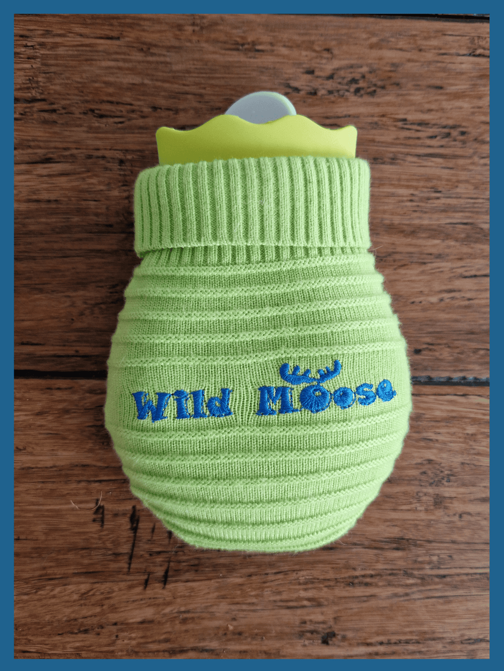 brightly coloured mini hot water bottle in a knitted cover in lime green against a wooden floor backdrop