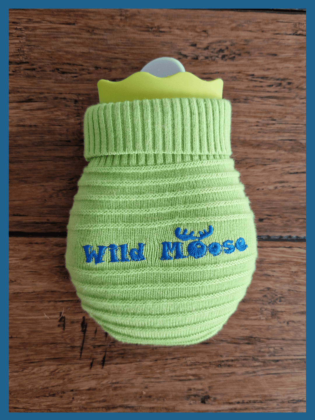 brightly coloured mini hot water bottle in a knitted cover in lime green against a wooden floor backdrop