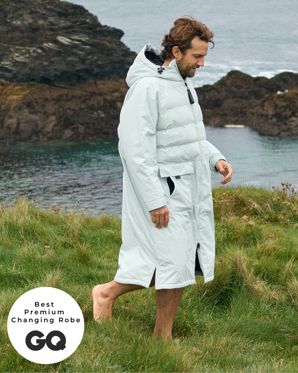 Lead_men - Man wearing a Vivida Lifestyle All Weather Puffer Changing Robe, Matcha Green Drying Robe for swimming standing on rocks. Sticker: Best Premium Changing Robe - The Independent.