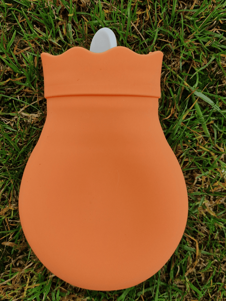 brightly coloured mini hot water bottle in orange on a grassy backdrop