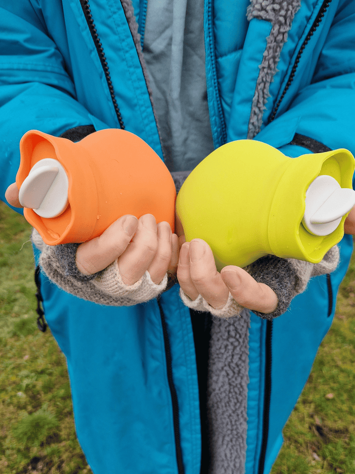 brightly coloured mini hot water bottles in orange and lime green held a lady wearing fingerless gloves