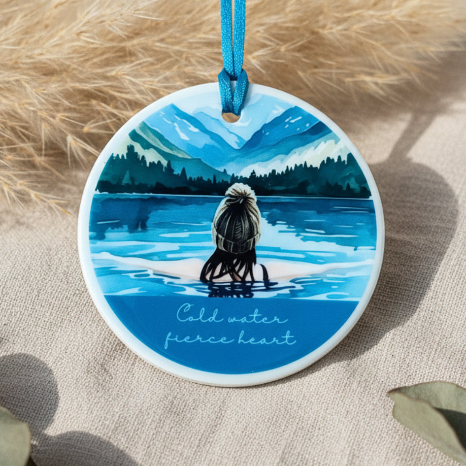Circular ornament with a painting of a person in a kayak on a lake, surrounded by mountains.