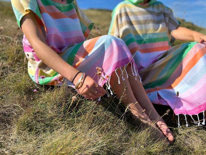 Two woman sitting on grass with one wearing the long version of the Breeze changing robe and the other the midi version