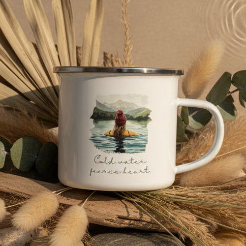 Enamel mug with a design of a person in water and mountains, text 'Cold water fierce heart' on a light blue background.