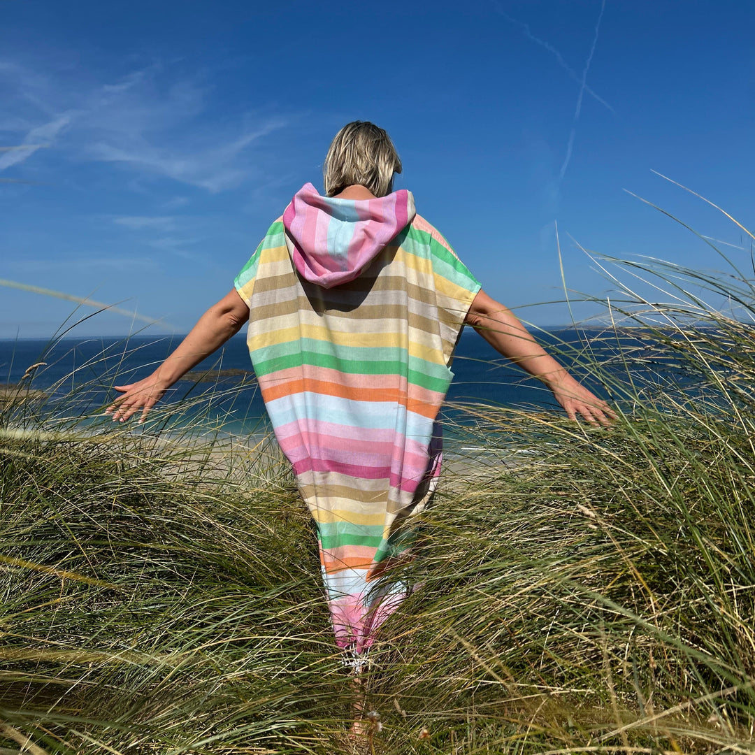 Person wearing a colorful striped dress standing in tall grass with a clear blue sky.