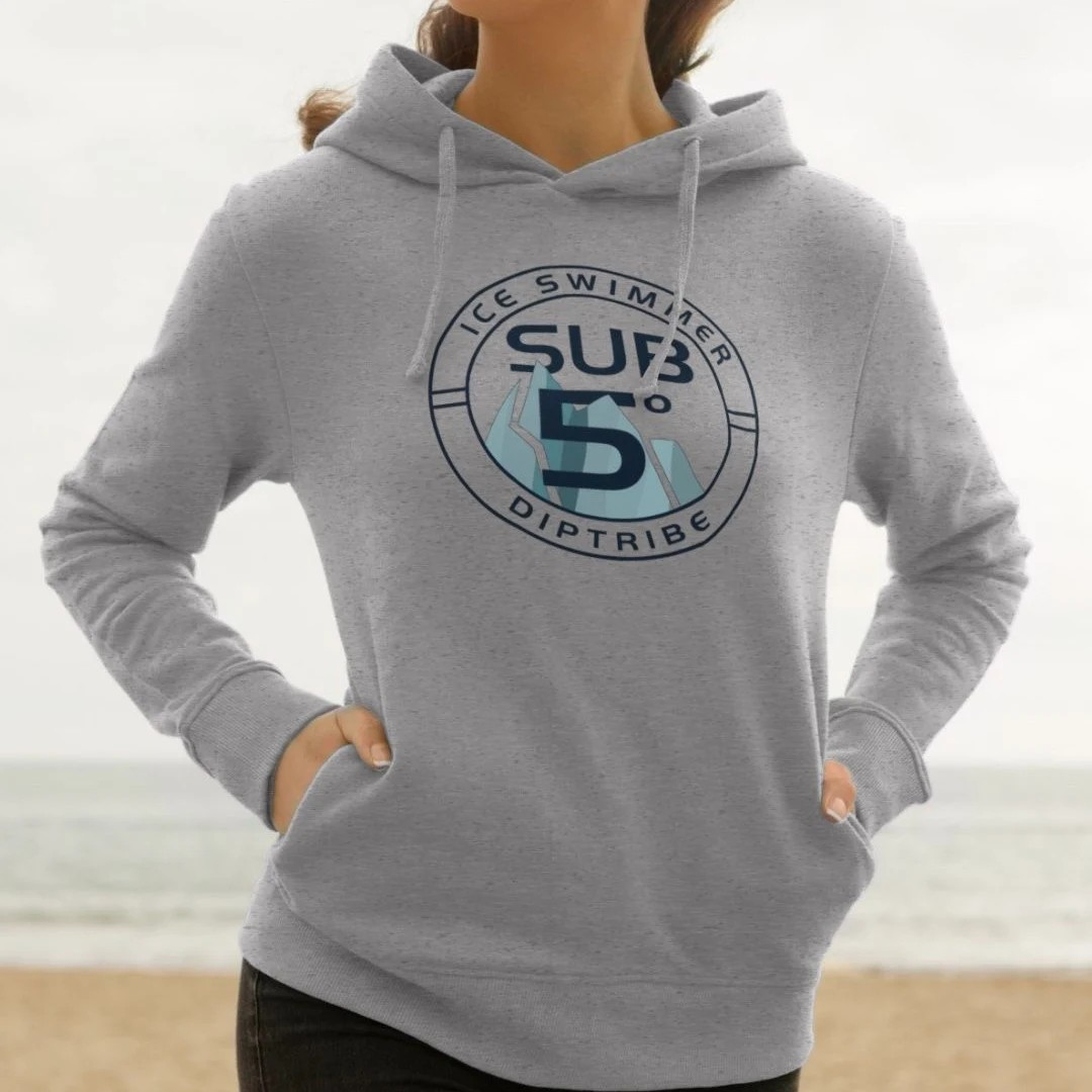 Lifestyle image of a woman on a beach wearing a grey diptribe hoodie with an 'Ice Swimmer Sub 5' circular logo on the front.