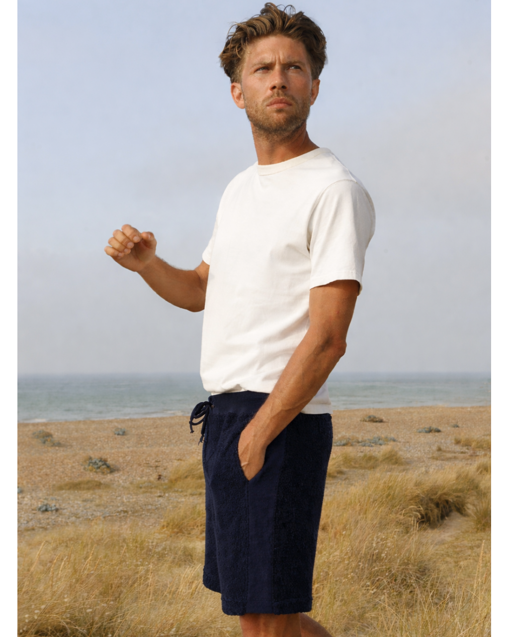 Man on the beach wearing navy So English Bear shorts, casual summer beachwear, made in the UK.