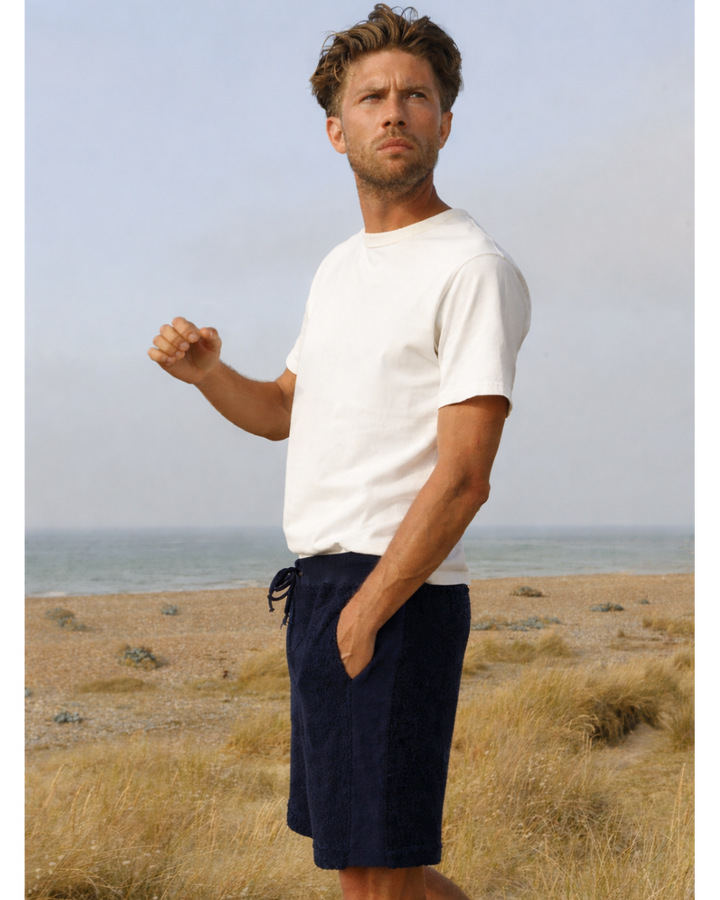 Man on the beach wearing navy So English Bear shorts, casual summer beachwear, made in the UK.