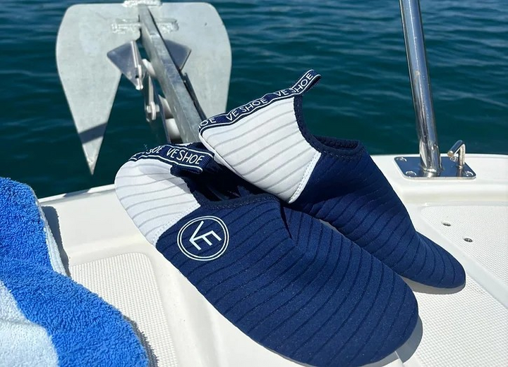 Lifestyle image of a pair of VE Shoe navy and white water shoes with white sole on the back deck of a boat