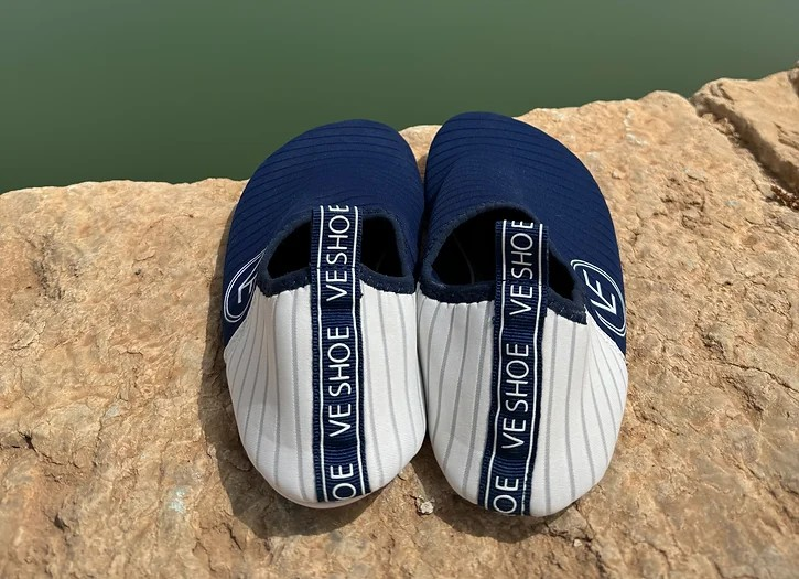 Lifestyle image of a pair of VE Shoe navy and white water shoes on a stone surface near the water