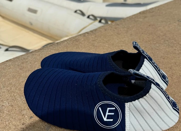 Lifestyle image of a pair of VE Shoe navy and white water shoes on a stone wall