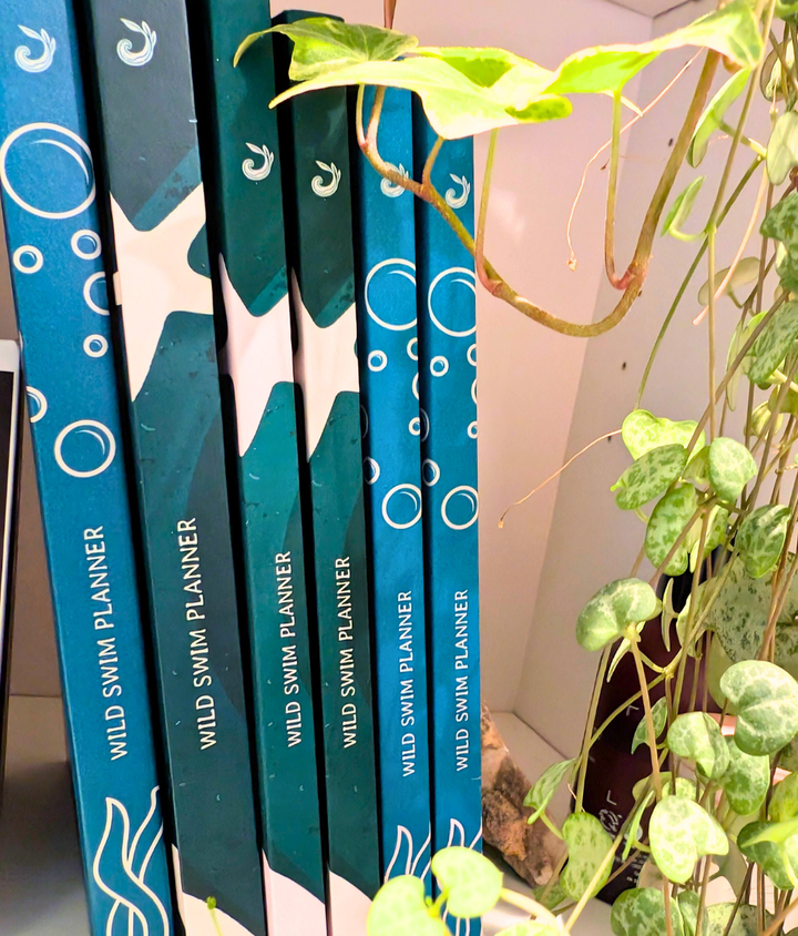 Blue and green wild swimming planners for open water swimmers sitting on a bookcase