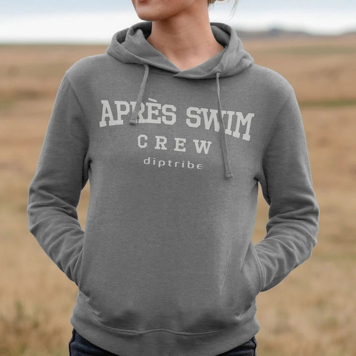 Lifestle image of a woman in a field wearing the diptribe light heather slim fit hoodie with an 'Apres Swim Crew' logo on the front