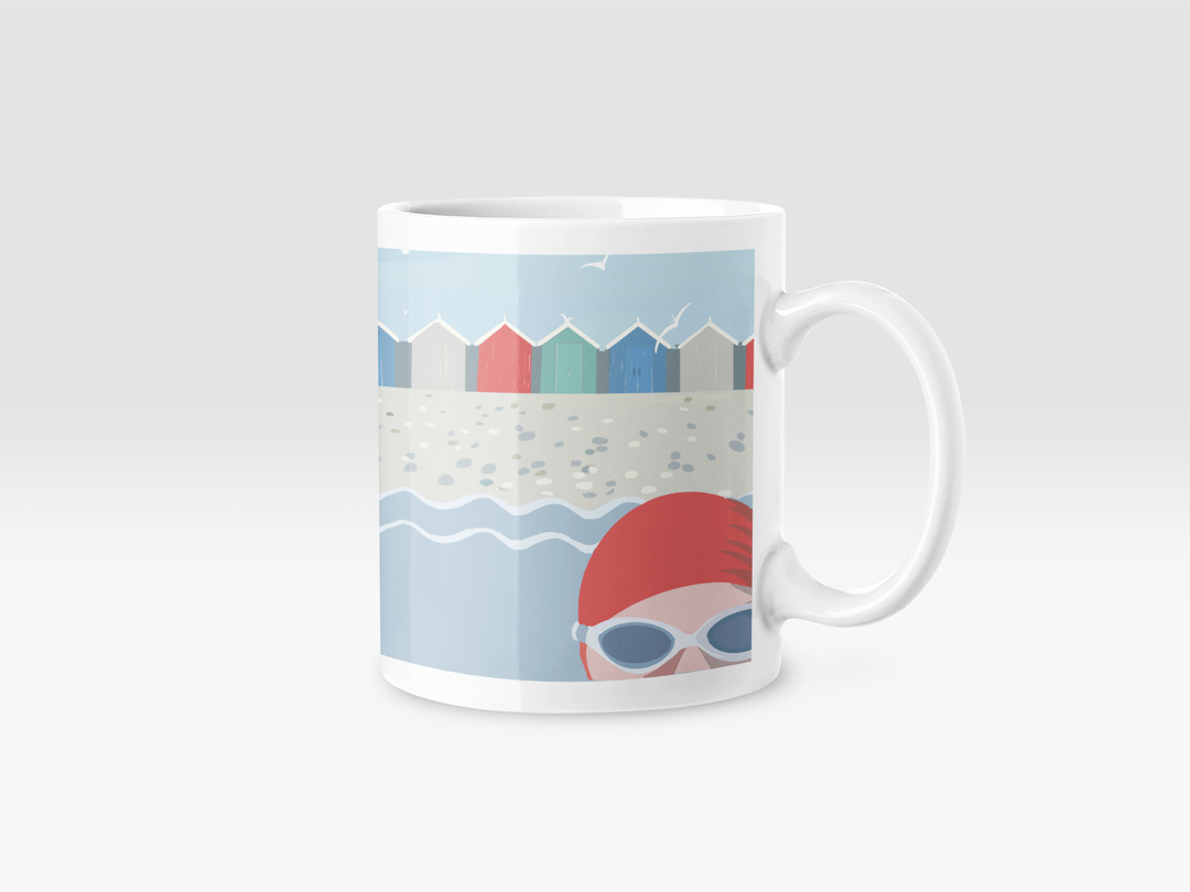 A white ceramic mug featuring a retro illustration of a swimmer in a red swimming cap and goggles in the sea, against a backdrop of colourful beach huts.
