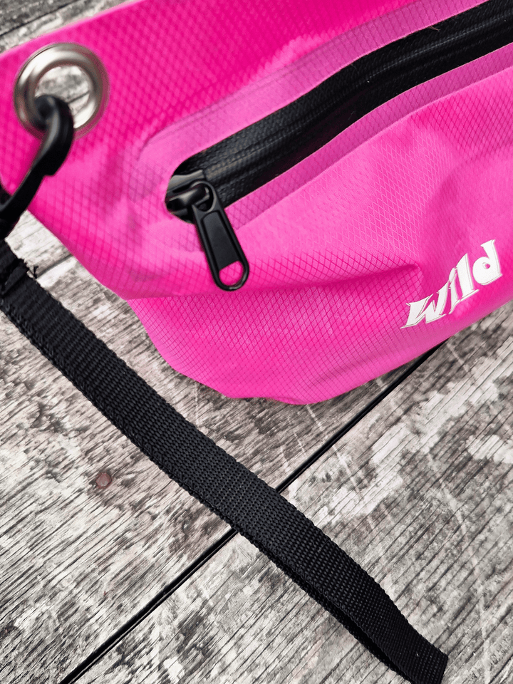 Pink zip bag with black wrist strap and 'Wild Moose' branding on a wooden surface