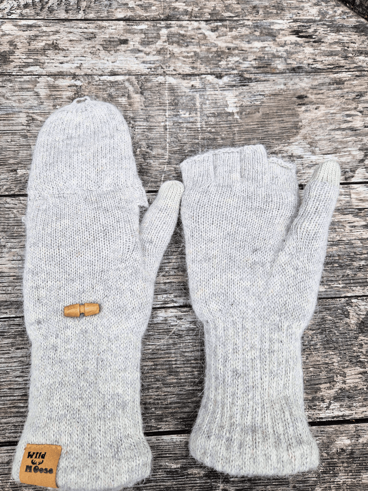 Pair of grey knit mittens on a wooden surface. One with mitten cover folded over and the other showing the fingerless gloves with the mitten cover folded back