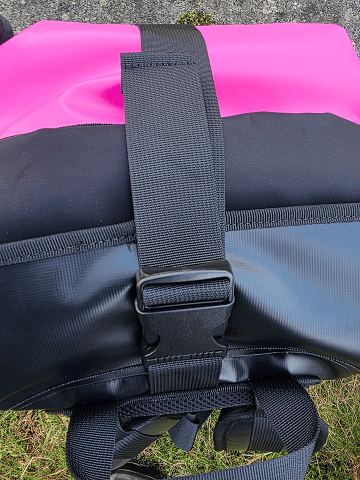 Black strap on a pink and black bag with grass in the background