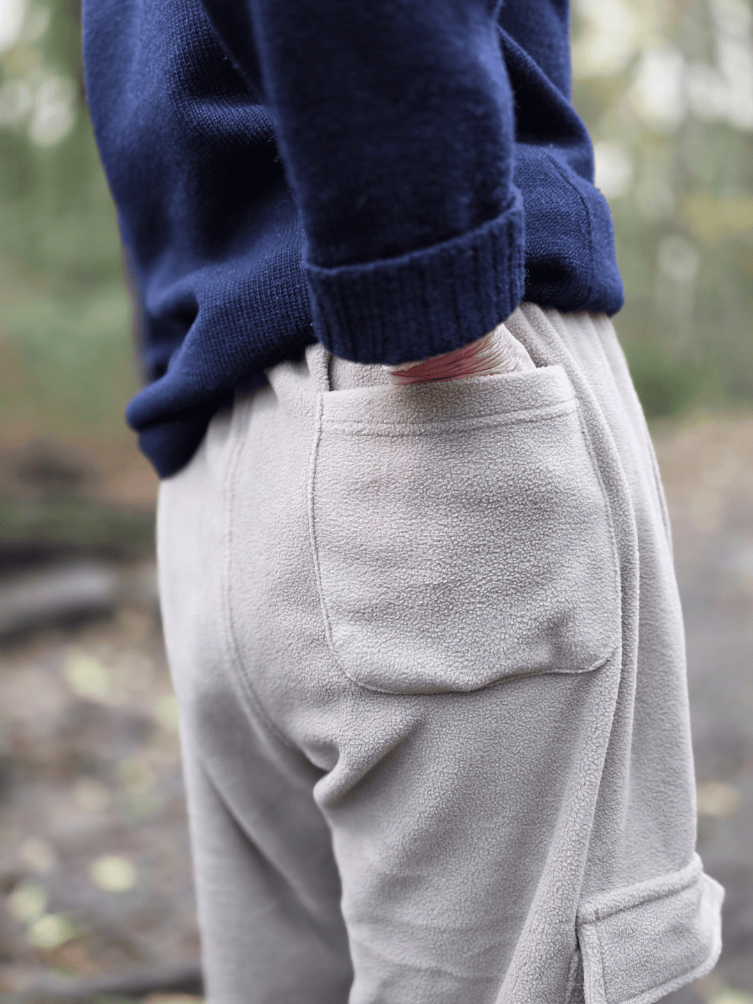 Person with hand in the back pocket of beige jogging pants with a blurred natural background