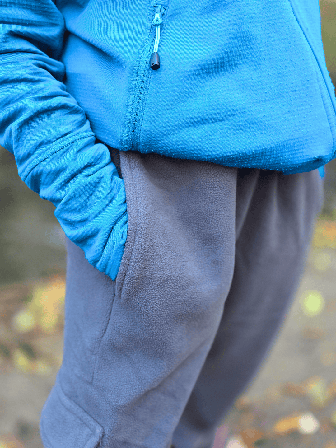 Person with hand in the side pocket of grey fleece jogging pants against a blurred natural background