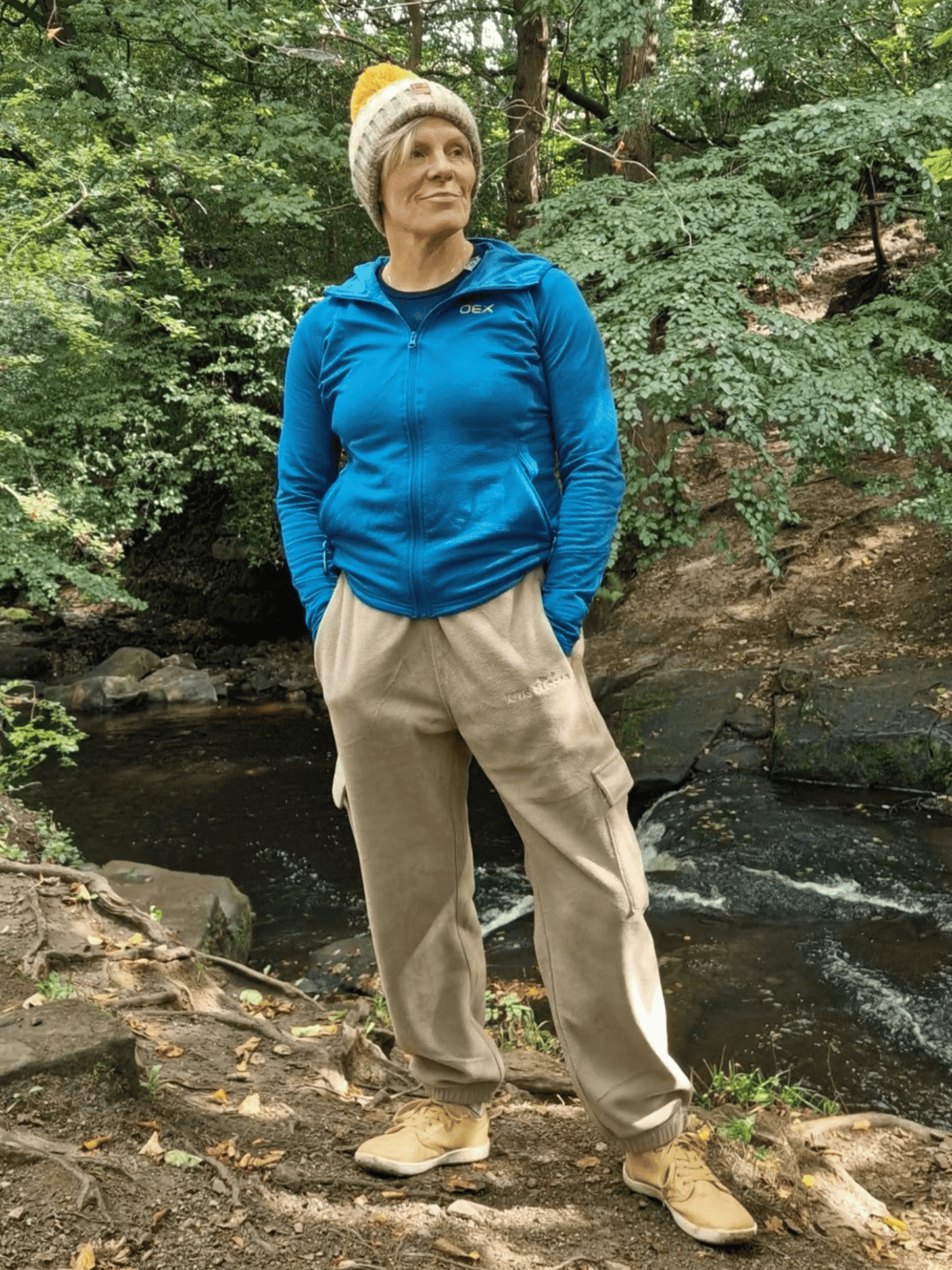 Person wearing beige fleece jogging pants standing by a stream in a forest.