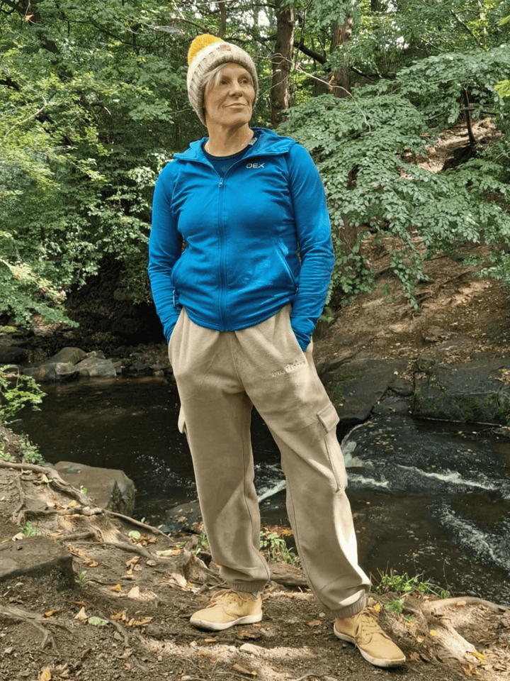Person wearing beige fleece jogging pants standing by a stream in a forest.