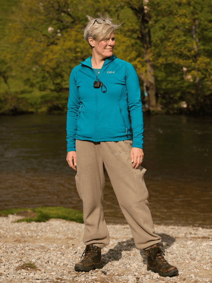 Person wearing beige fleece jogging pants  standing by a body of water with trees in the background.