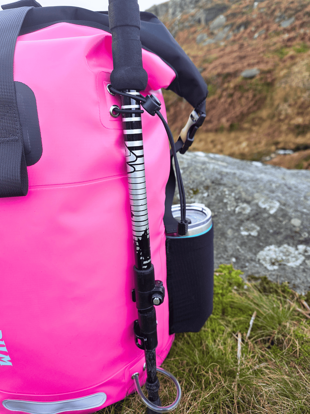 Pink dry bag with a backpack strap and a cup holding side pocket, outdoors.