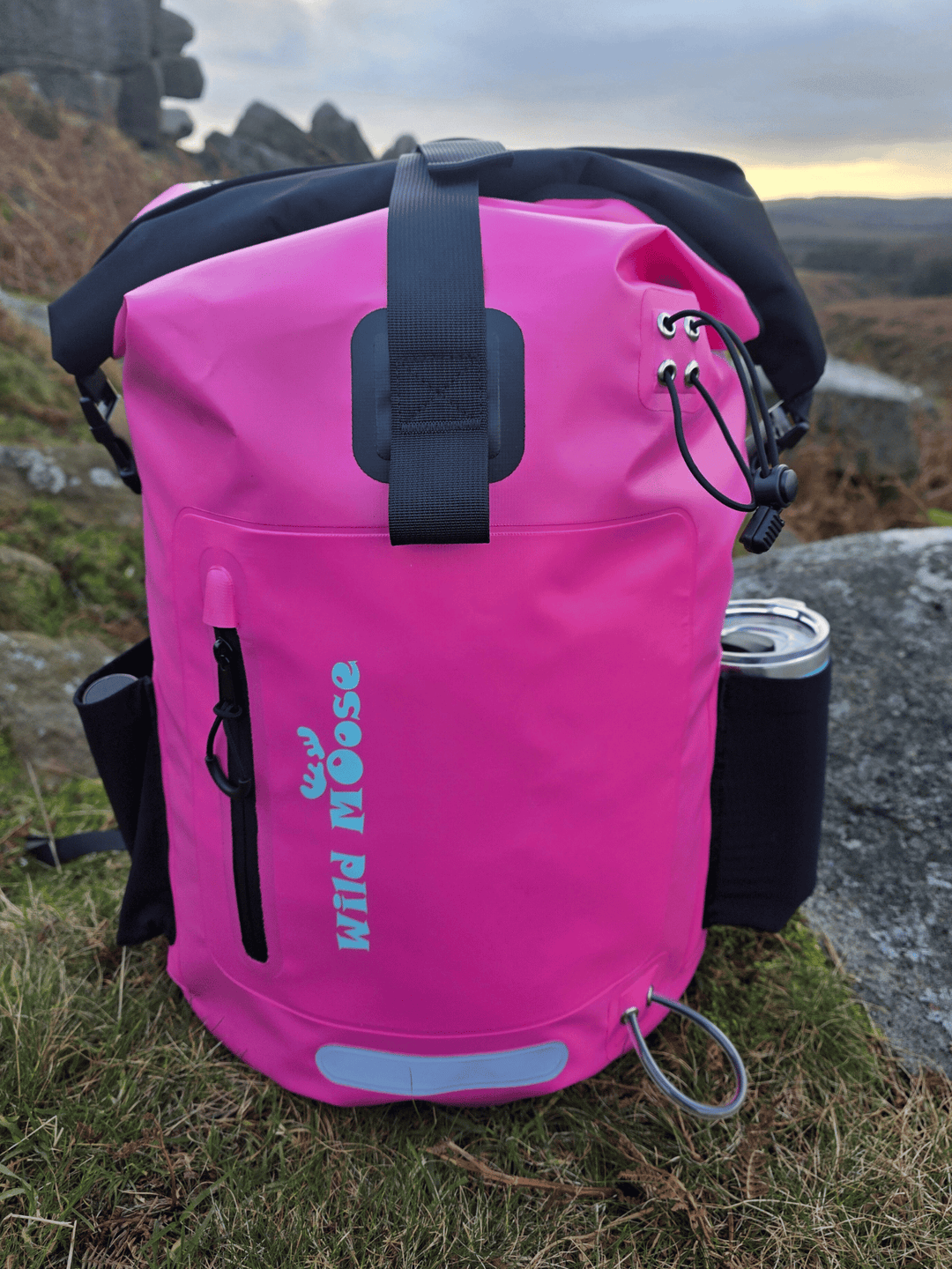 Pink waterproof bag with 'Wild Moose' branding on a grassy hillside.