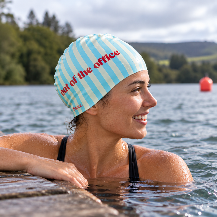 Female swimmer in a lake wearing a blue striped Out of the Office silicone swimming cap.
