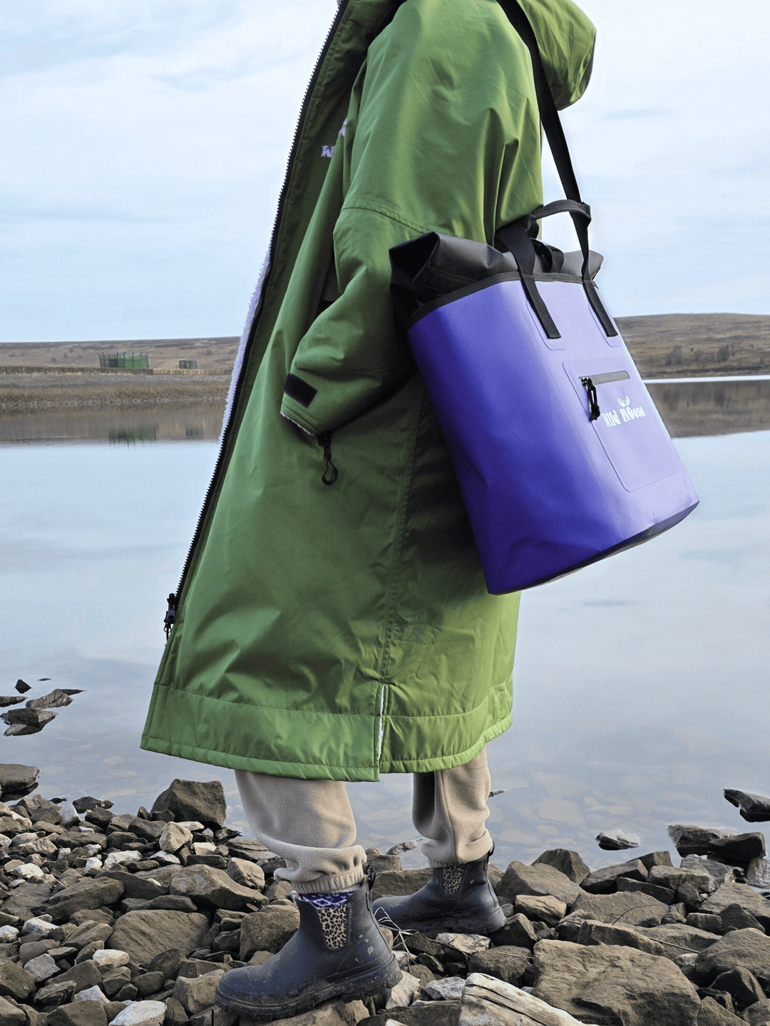 lady with purple tote bag over shoulder wearing a green robe looking at a rocky lake