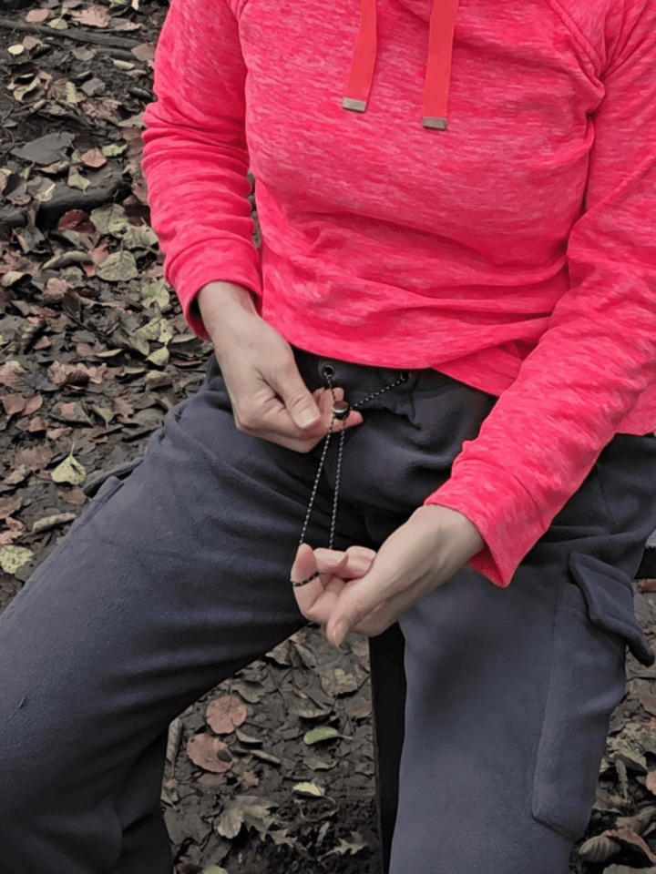 Person wearing dark grey fleece jogging pants sitting on a bench and pulling the drawstring fastening.