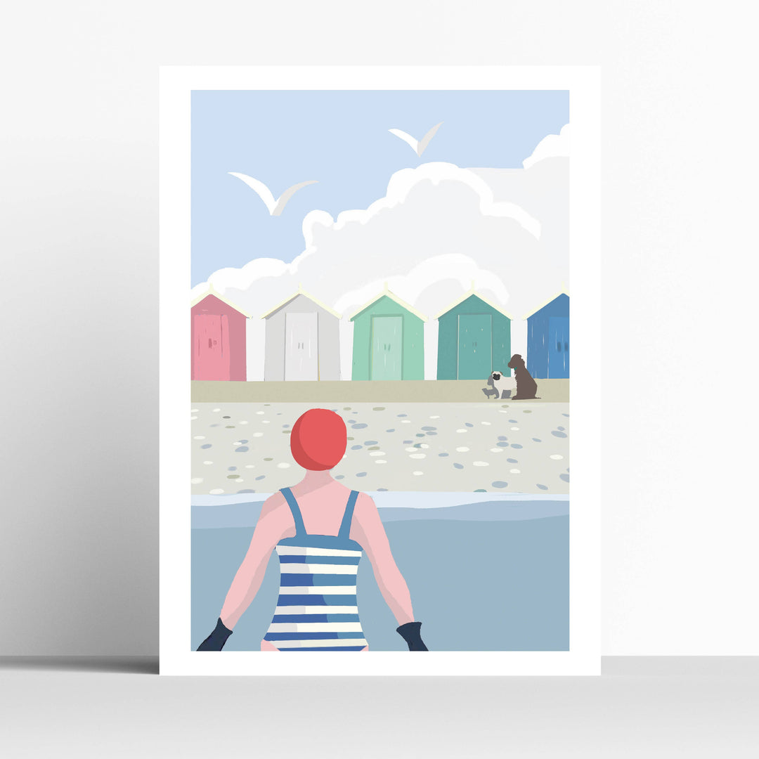 An A4 art print featuring a minimalist beach illustration. The print depicts a swimmer in a blue and white stripey swimsuit with a red swim cap, facing a row of colorful beach huts under a light blue sky with white clouds and seagulls.