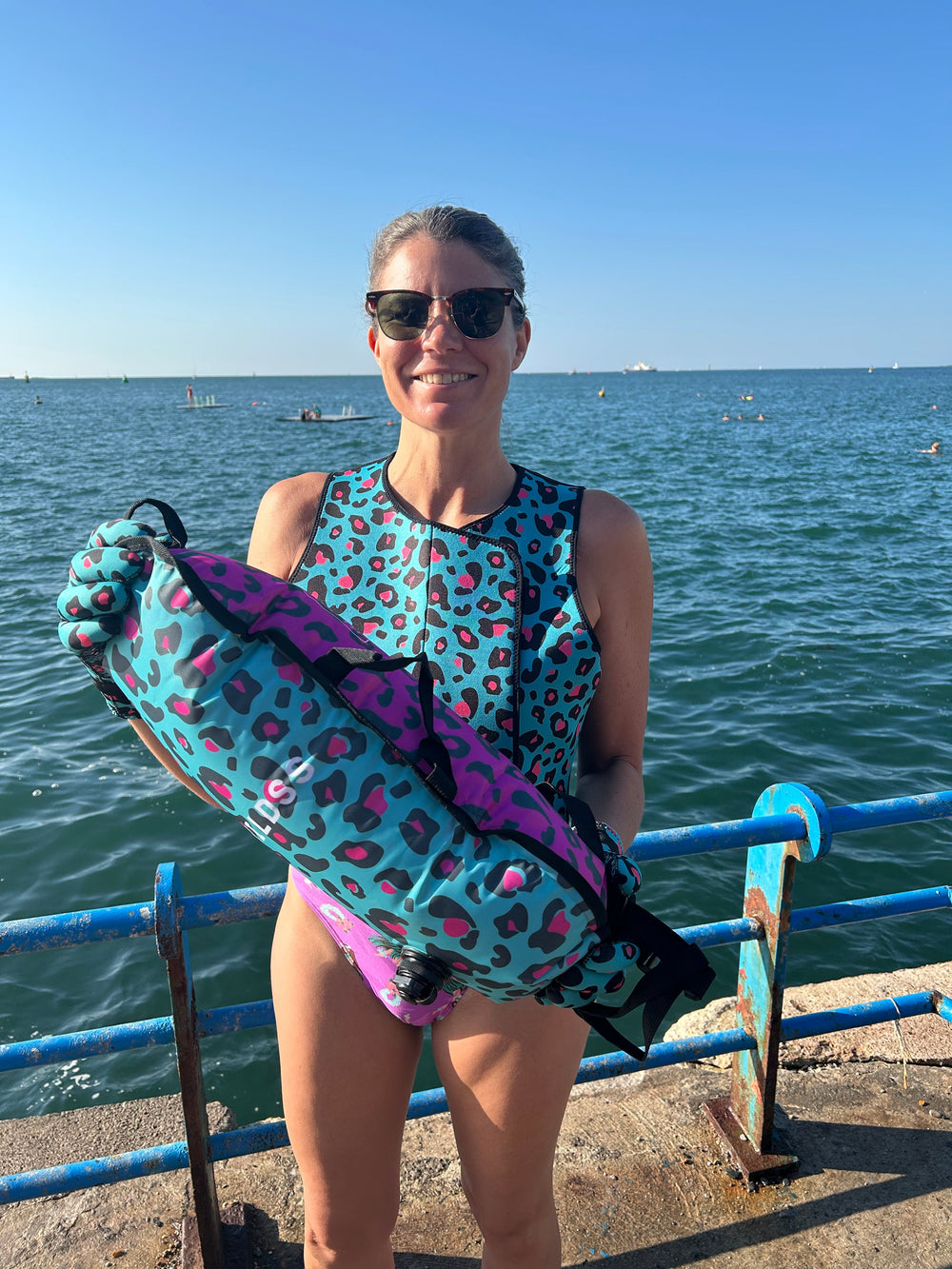 Swimmer standing on water's edge holding leopard print tow float with built-in thermometer.