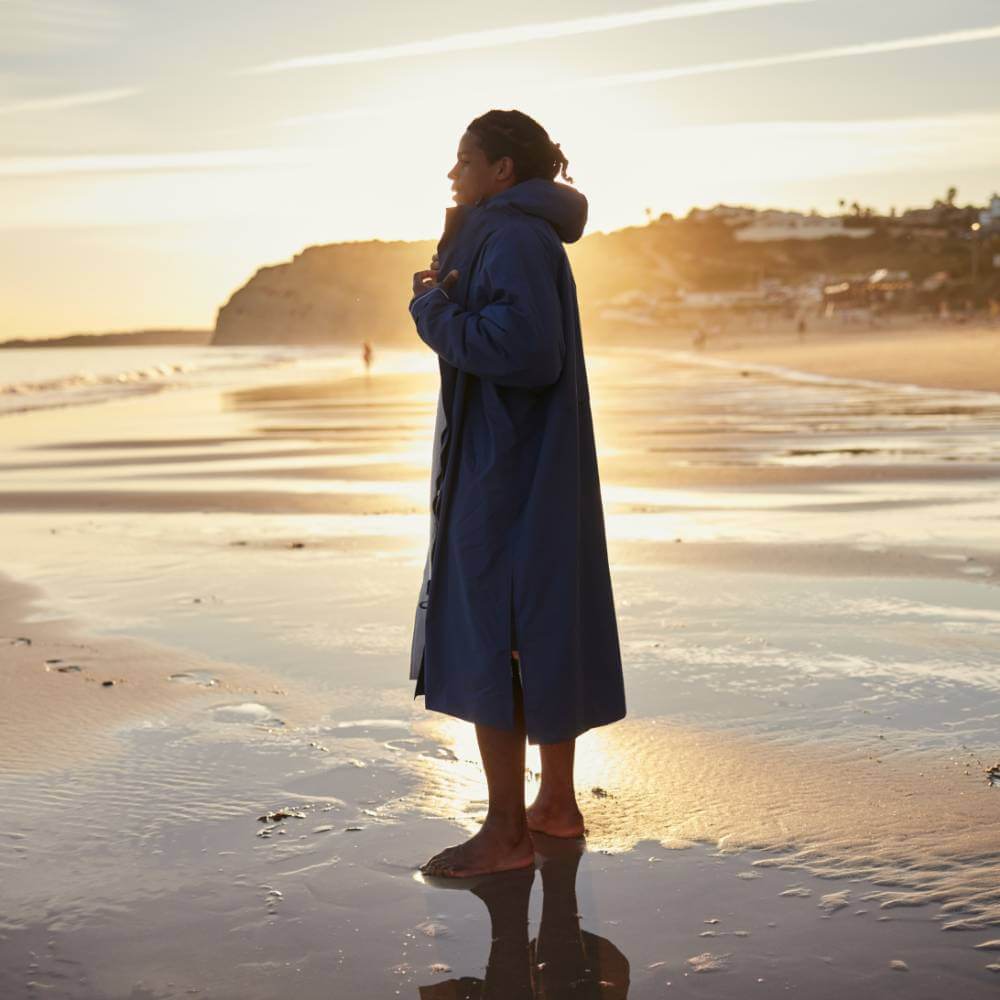 Swimmer wearing a Red Alter Evo men’s long sleeve waterproof changing robe in Admiral Blue on the beach after a cold water swim.