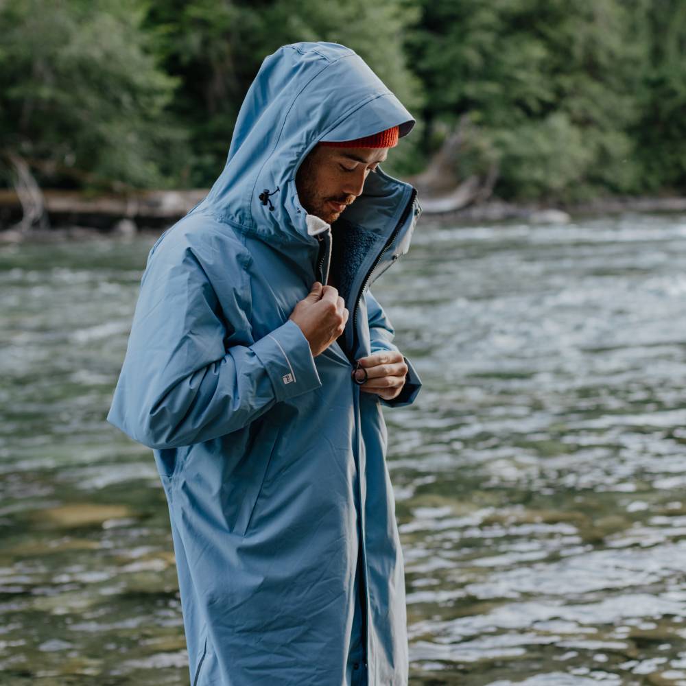 Swimmer wearing a Red Alter Evo men’s long sleeve waterproof changing robe in Alpine Blue by a river after a cold water swim.