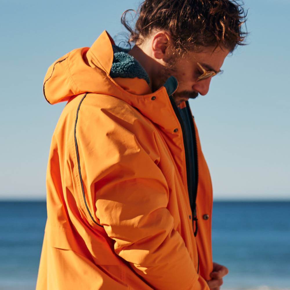 Swimmer wearing a Red Alter Evo men’s long sleeve waterproof changing robe in Bitter Orange on the beach after a cold water swim.