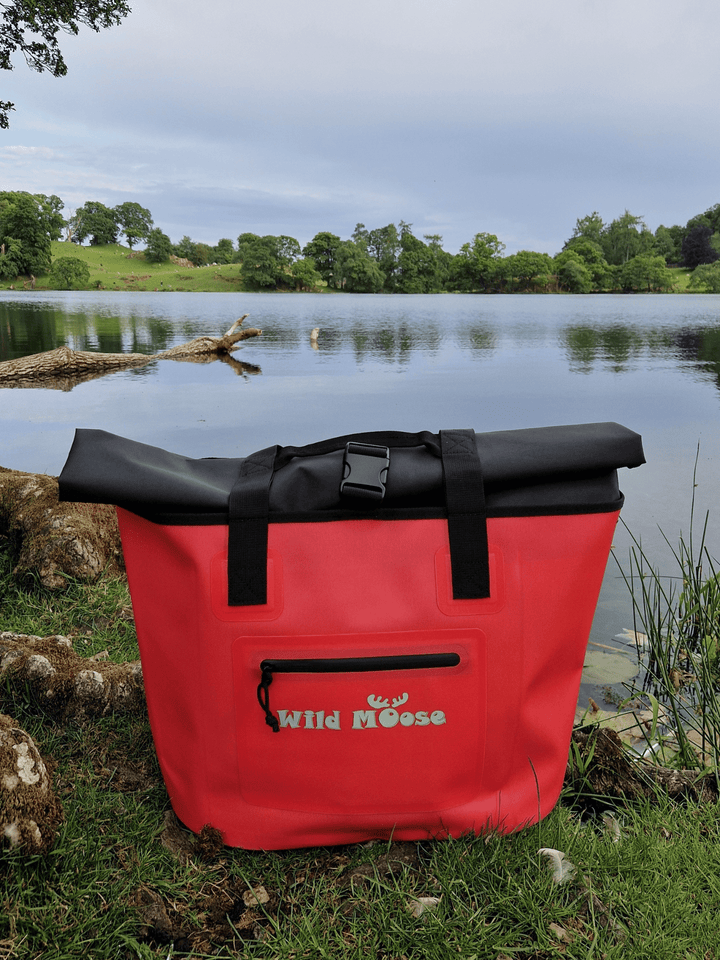 Product shot of a coral coloured Wild Moose tote bag on the shores of a Lakeland tarn. The roll-top design ensures your kit will stay fully dry