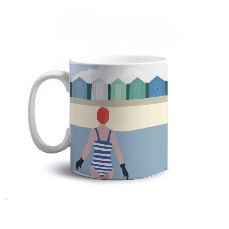 A white ceramic mug featuring a beach illustration with colourful beach huts, and a swimmer in a blue-and-white striped swimsuit in the sea.