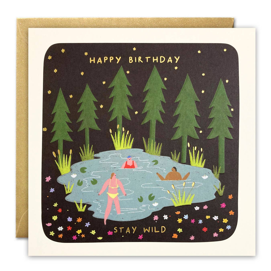 Stay Wild swimming birthday card illustrated by Sarah Wilson featuring wild swimmers in a lake beneath pine trees with gold foil Happy Birthday lettering.