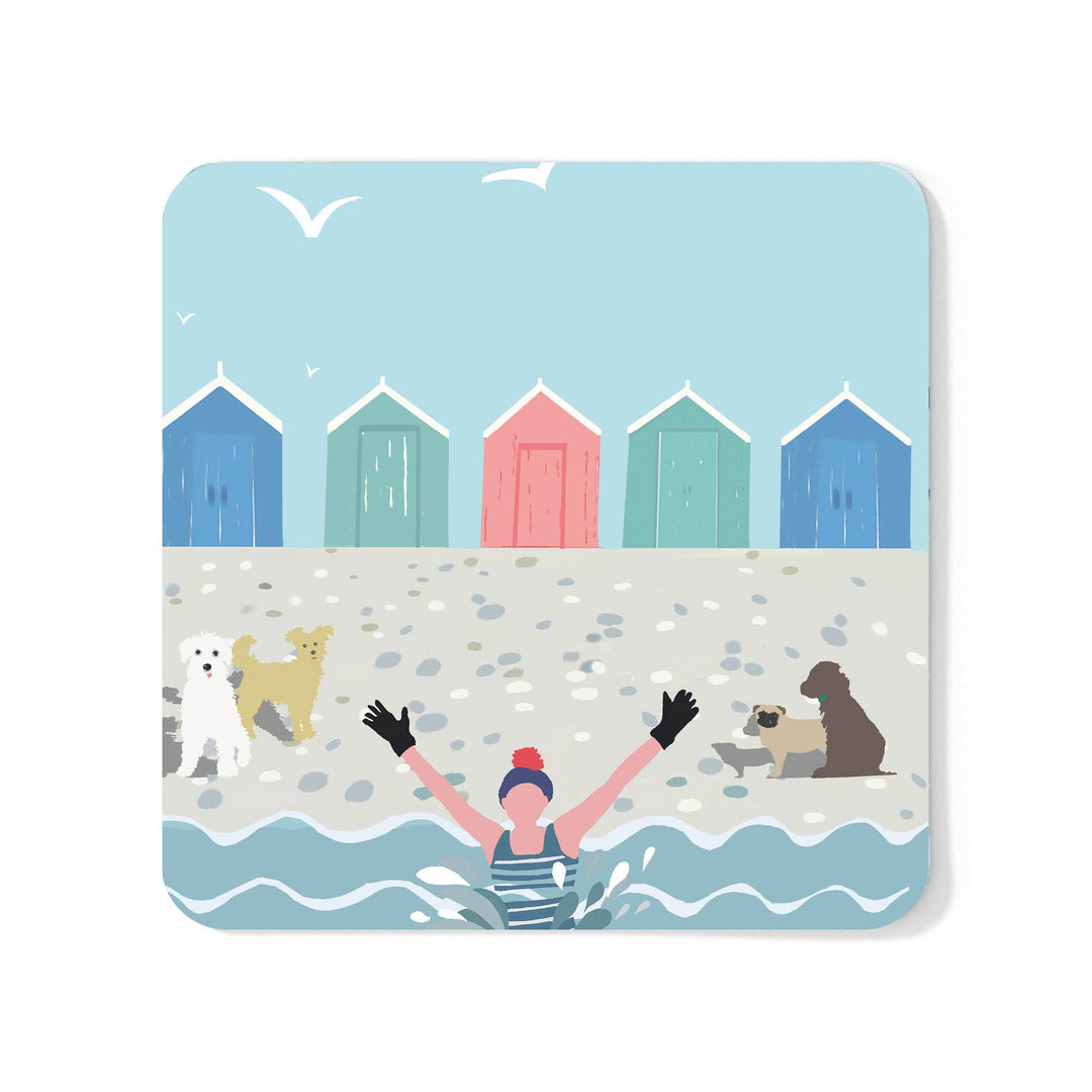 A square coaster with rounded corners featuring a colourful beach illustration. The design shows five beach huts, a person in the water and four dogs on the sandy beach.