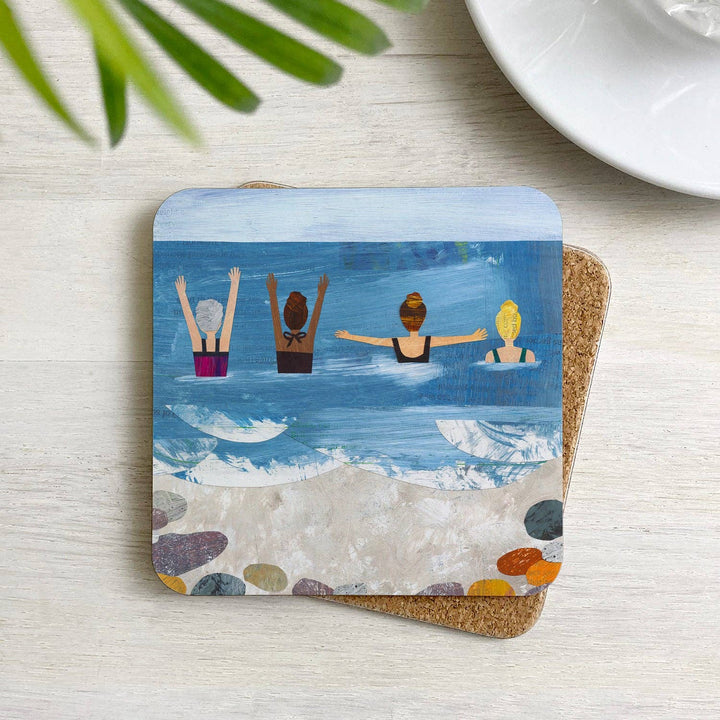 Wild Sea Swimmers cork-backed coaster with an illustration featuring four swimmers in the ocean displayed on a table in a home setting.