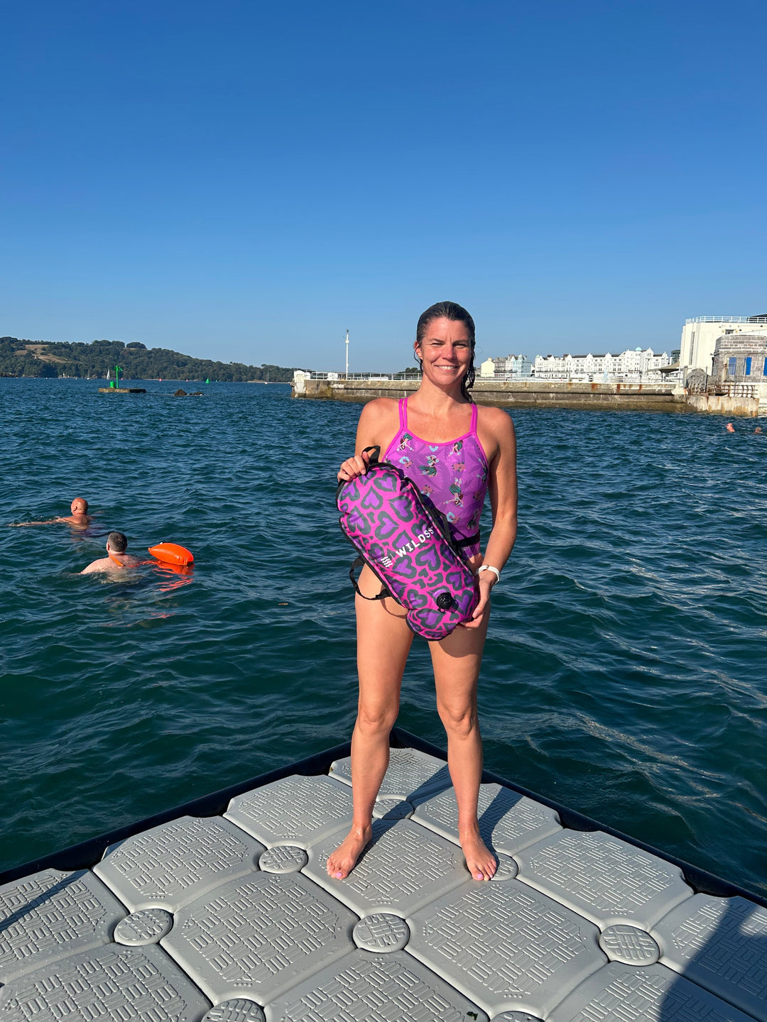 Open water swimmer standing by the water with a Wild Swimming Socks 'Cold Cold Heart' design swim bouy with built-in thermometer.