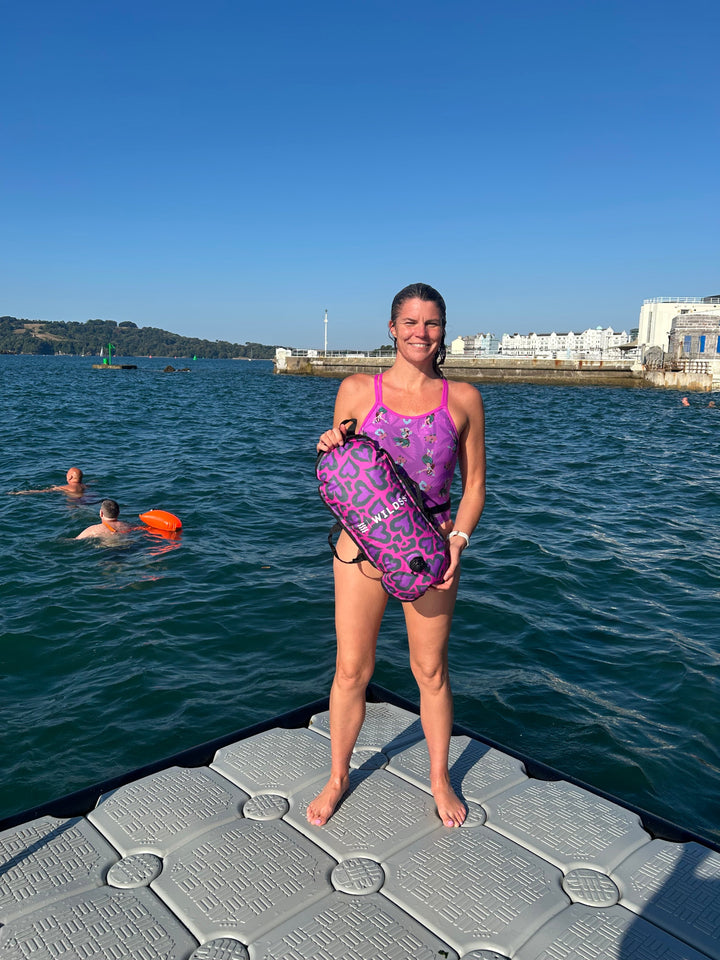 Open water swimmer standing by the water with a Wild Swimming Socks 'Cold Cold Heart' design swim bouy with built-in thermometer.