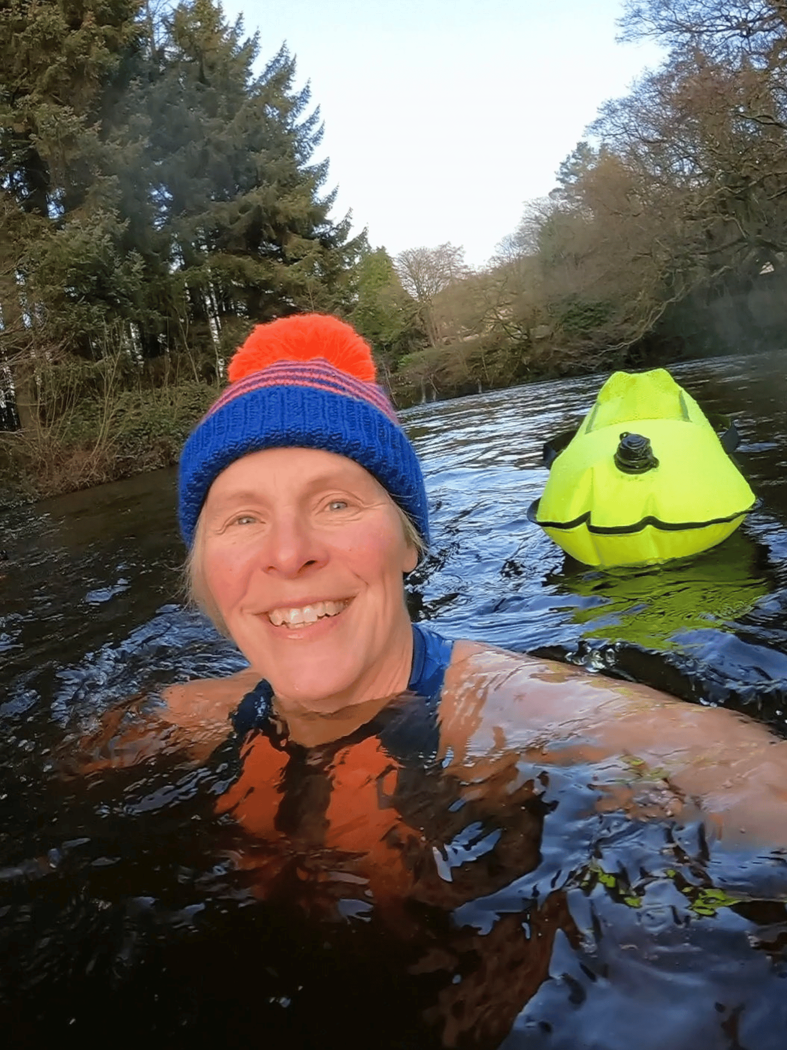 lady swimming in a bright, stripey hat with a neon yellow tow float behind
