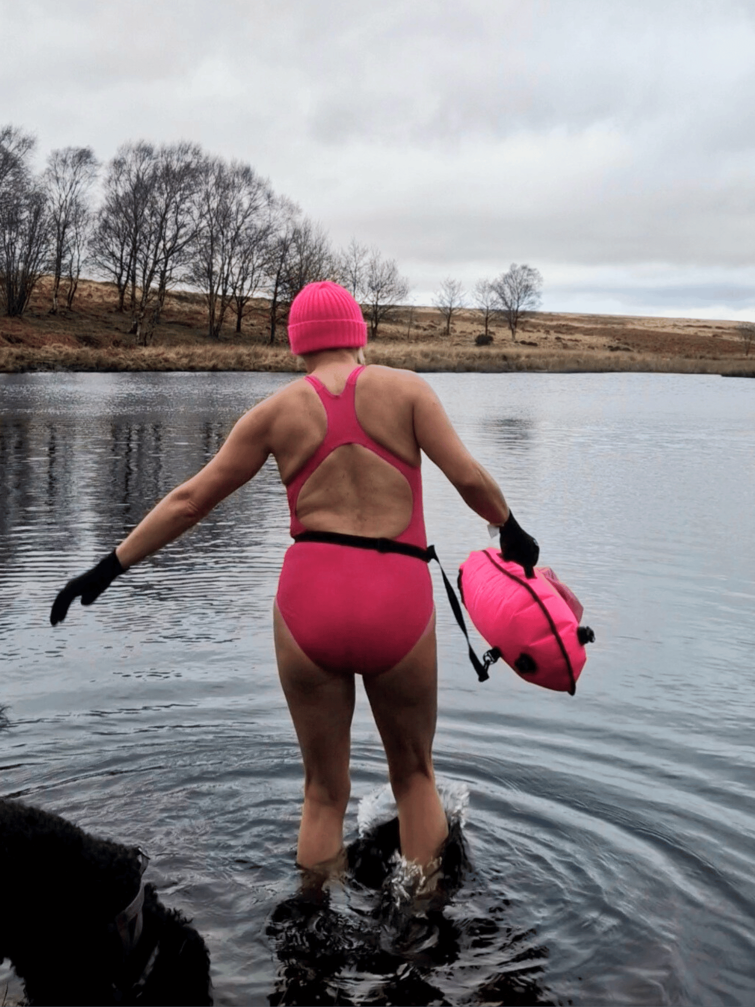 lady in pink hat, pink costume and carrying a  pink tow float making her way into a lake 